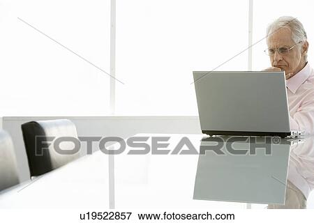 Stock Photo - Senior businessman using laptop at conference table. Fotosearch