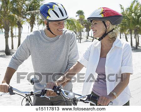 Stock Image - Senior couple on bicycles on tropical beach. Fotosearch