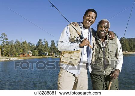 Senior man and son holding fishing rods by lake smiling (portrait) View Large Photo Image Stock Image - Senior man and son holding fishing rods by lake smiling (portrait). Fotosearch