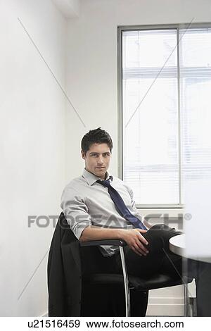 Serious Businessman sitting at desk in office portrait View Large Photo Image Stock Photo - Serious Businessman sitting at desk in office portrait. Fotosearch