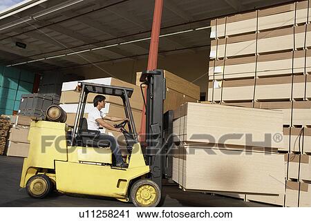 Stock Image - Side view of male worker operating forklift vehicle. Fotosearch