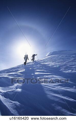 Stock Image - Skiers hiking to mountain summit. Fotosearch