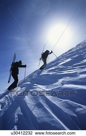 Stock Image - Skiers hiking to mountain summit. Fotosearch