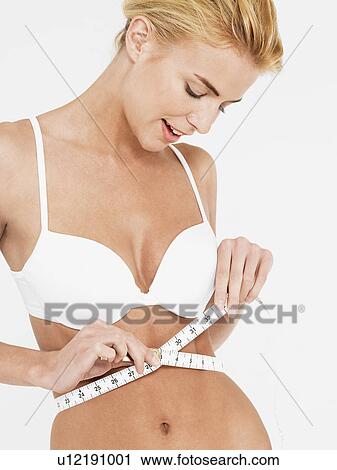 Stock Image - Slender young woman in white bra measuring her waist. Fotosearch