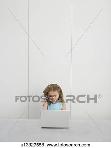 Small girl by desk using cell phone and laptop View Large Photo Image Stock Photo - Small girl by desk using cell phone and laptop. Fotosearch