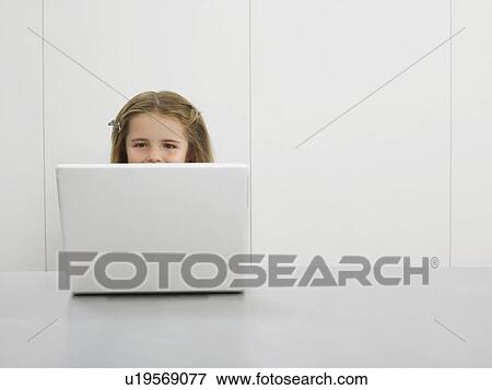 Stock Photo - Small girl by desk using laptop. Fotosearch