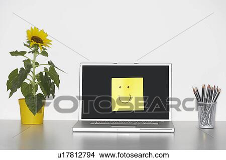 Smiley face on laptop by pencils in cup and flowers on desk View Large Photo Image Picture - Smiley face on laptop by pencils in cup and flowers on desk. Fotosearch