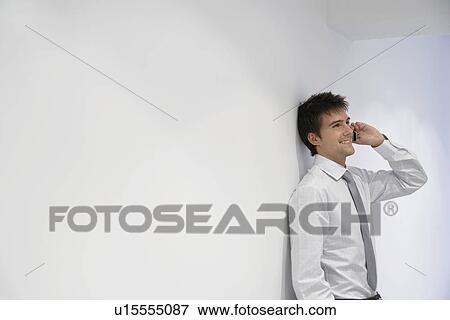 Smiling Businessman leaning on wall Talking on Cell Phone View Large Photo Image Stock Photo - Smiling Businessman leaning on wall Talking on Cell Phone. Fotosearch