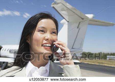 Smiling Businesswoman standing outside Airplane talking on mobile View Large Photo Image Stock Photo - Smiling Businesswoman standing outside Airplane talking on mobile. Fotosearch