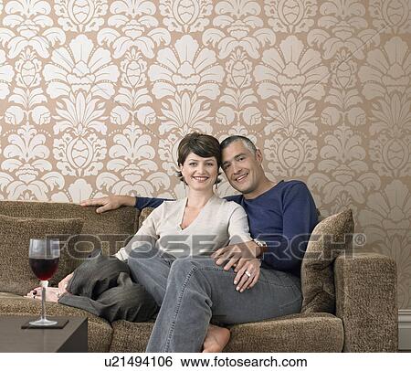 Stock Photograph - Smiling couple relaxing on sofa in living room (portrait). Fotosearch