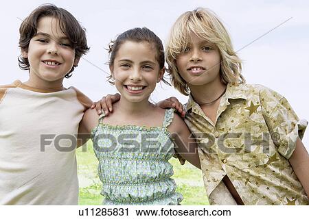 Stock Image - Smiling pre-teen Friends standing side by side outside arms around. Fotosearch