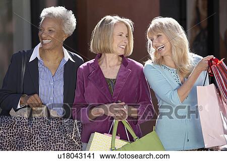 Stock Image - Smiling Women walking outside carrying bags on Shopping Trip. Fotosearch