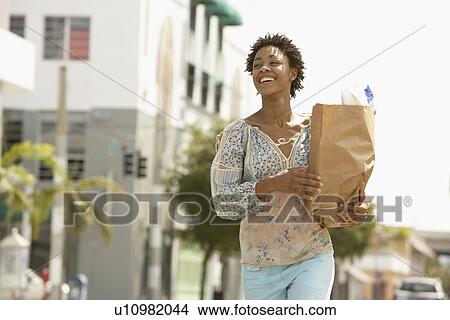 Picture - Smiling young woman carrying groceries portrait. Fotosearch