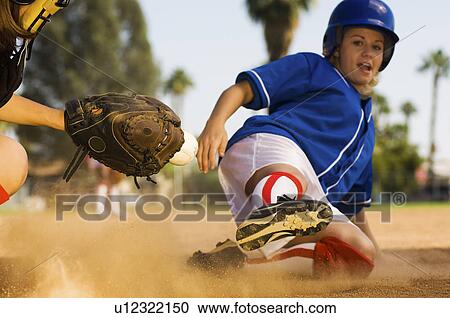 Stock Image - Softball player sliding into home plate. Fotosearch