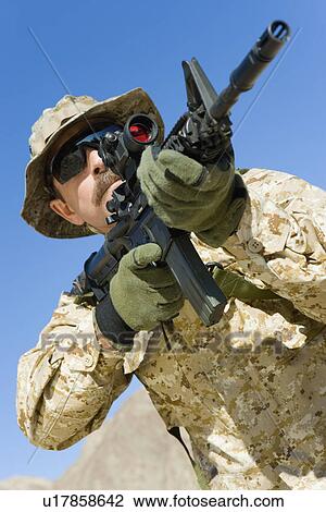 Stock Image - Soldier aiming rifle outdoors (low angle view). Fotosearch