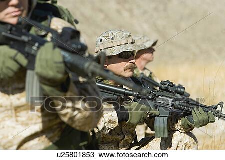 Stock Image - Soldiers aiming rifles in field. Fotosearch