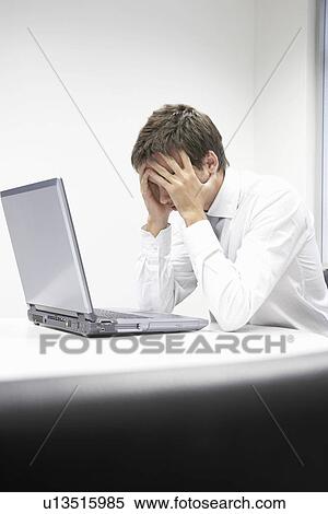 Stressed businessman sitting at desk with laptop View Large Photo Image Stock Photography - Stressed businessman sitting at desk with laptop. Fotosearch