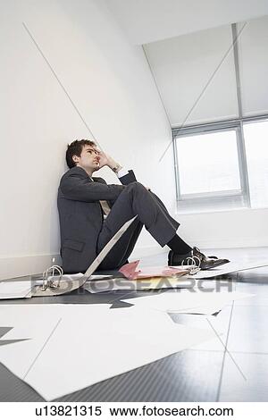 Stock Photography - Stressed businessman sitting on floor of empty office by scattered files. Fotosearch