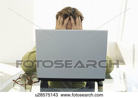Stock Image - Stressed businessman using laptop in office. Fotosearch