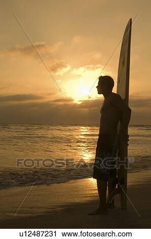 Surfer standing on beach leaning on surfboard watching sunset side view View Large Photo Image Stock Image - Surfer standing on beach leaning on surfboard watching sunset side view. Fotosearch