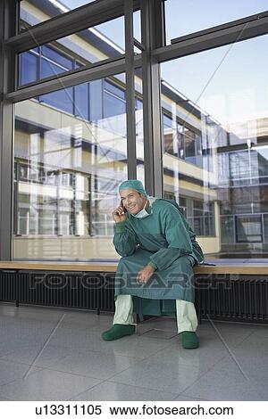Stock Photography - Surgeon sitting in hospital corridor using mobile phone. Fotosearch