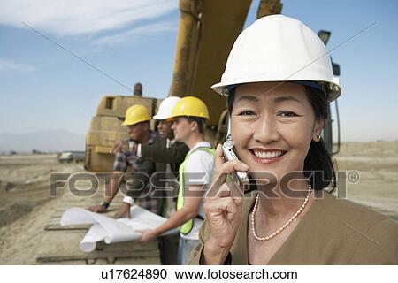 Surveyor in hard hat standing in front of heavy machinery Using Cell Phone on Construction Site View Large Photo Image Stock Image - Surveyor in hard hat standing in front of heavy machinery Using Cell Phone on Construction Site. Fotosearch