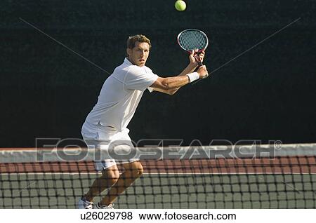 Tennis Player squatting on tennis court Hitting Backhand over net View Large Photo Image Stock Photo - Tennis Player squatting on tennis court Hitting Backhand over net. Fotosearch