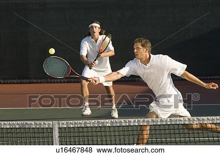 Tennis Player stretching Swinging at Ball near tennis net doubles partner standing behind View Large Photo Image Stock Photo - Tennis Player stretching Swinging at Ball near tennis net doubles partner standing behind. Fotosearch