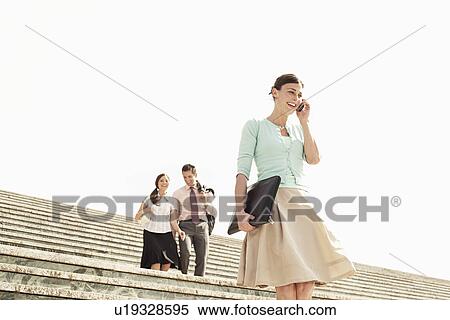 Stock Photography - Three office workers walking down steps woman in foreground using mobile phone low angle view.. Fotosearch