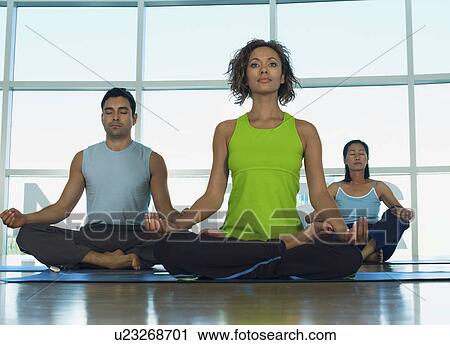 Stock Image - Three people doing yoga indoors. Fotosearch