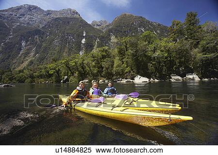 Stock Photography - Three people paddling kayaks in mountain lake. Fotosearch