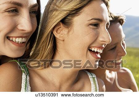 Stock Image - Three young women sitting in mountain field looking at view close up. Fotosearch