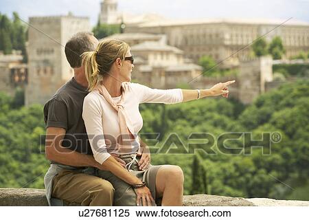 Tourist Couple sitting on Wall in Granada Spain looking and pointing at view View Large Photo Image Stock Photography - Tourist Couple sitting on Wall in Granada Spain looking and pointing at view. Fotosearch