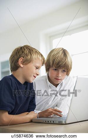 Stock Photograph - Two brothers using laptop on table at home. Fotosearch