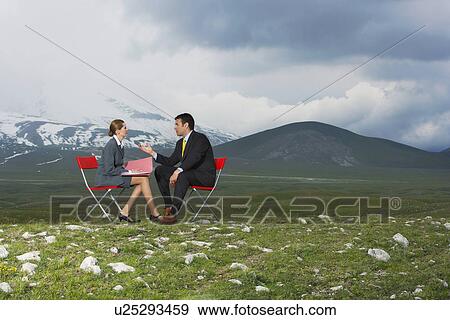 Stock Photo - Two business people sitting and talking in mountain field side view. Fotosearch