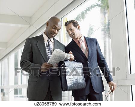 Two businessmen discussing financial pages in modern hallway View Large Photo Image Stock Photo - Two businessmen discussing financial pages in modern hallway. Fotosearch