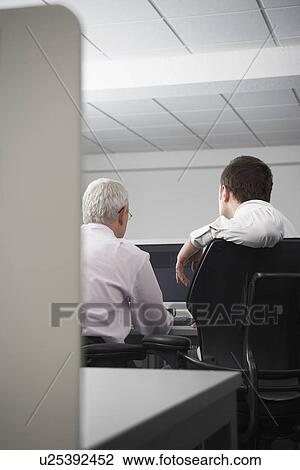 Two businessmen using computer in office cubicle back view View Large Photo Image Stock Image - Two businessmen using computer in office cubicle back view. Fotosearch