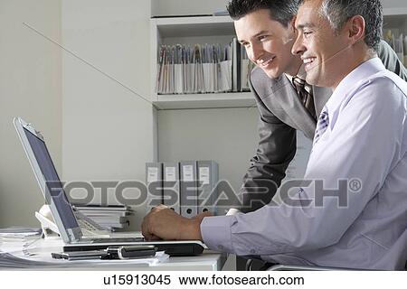 Two businessmen using laptop at office desk View Large Photo Image Stock Photography - Two businessmen using laptop at office desk. Fotosearch