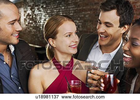 Stock Photo - Two couples laughing holding drinks in bar. Fotosearch