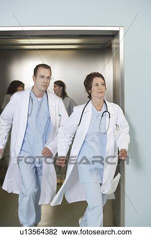 Stock Image - Two doctors running out of elevator. Fotosearch