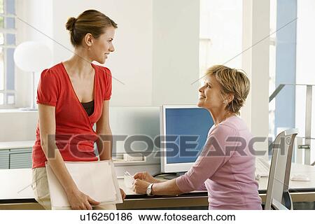 Stock Photograph - Two female office workers talking at cubicle. Fotosearch