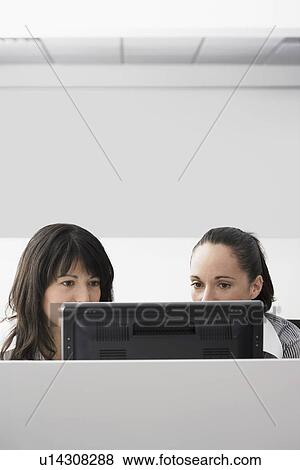 Two female office workers using computer in office cubicle View Large Photo Image Stock Photo - Two female office workers using computer in office cubicle. Fotosearch