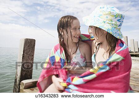 Two girls wrapped in towel sitting together at end of pier View Large Photo Image Stock Image - Two girls wrapped in towel sitting together at end of pier. Fotosearch