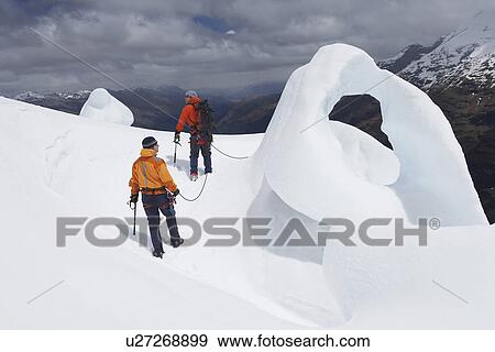 Two hikers going past ice formation in mountains back view View Large Photo Image Stock Photo - Two hikers going past ice formation in mountains back view. Fotosearch