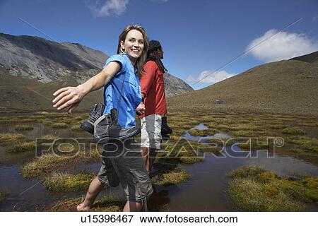 Two hikers holding hands wading through pond between hills View Large Photo Image Stock Photo - Two hikers holding hands wading through pond between hills. Fotosearch