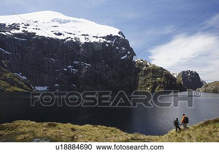 Stock Image - Two hikers looking at mountain lake. Fotosearch
