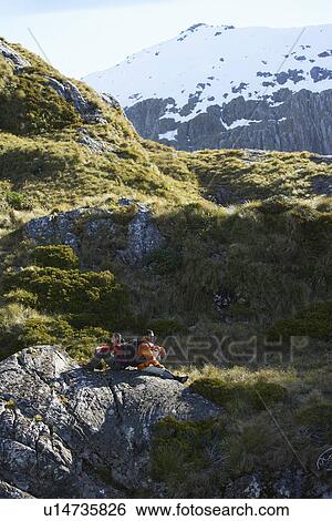 Two hikers sitting on boulders in mountain valley View Large Photo Image Stock Photograph - Two hikers sitting on boulders in mountain valley. Fotosearch