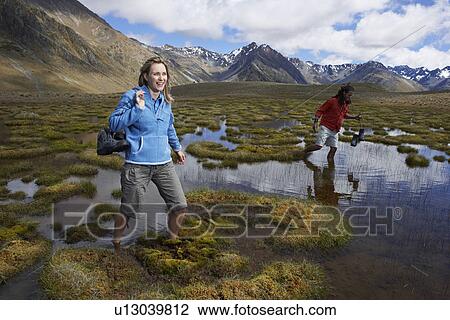 Two hikers wading through pond by mountains View Large Photo Image Stock Image - Two hikers wading through pond by mountains. Fotosearch