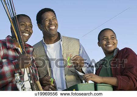 Stock Photograph - Two men and boy preparing to fly fishing smiling (low angle view). Fotosearch
