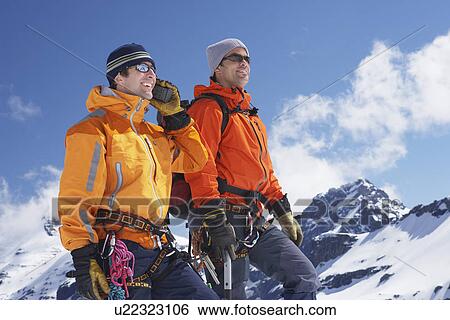 Two mountain climbers standing on peak View Large Photo Image Stock Photograph - Two mountain climbers standing on peak. Fotosearch